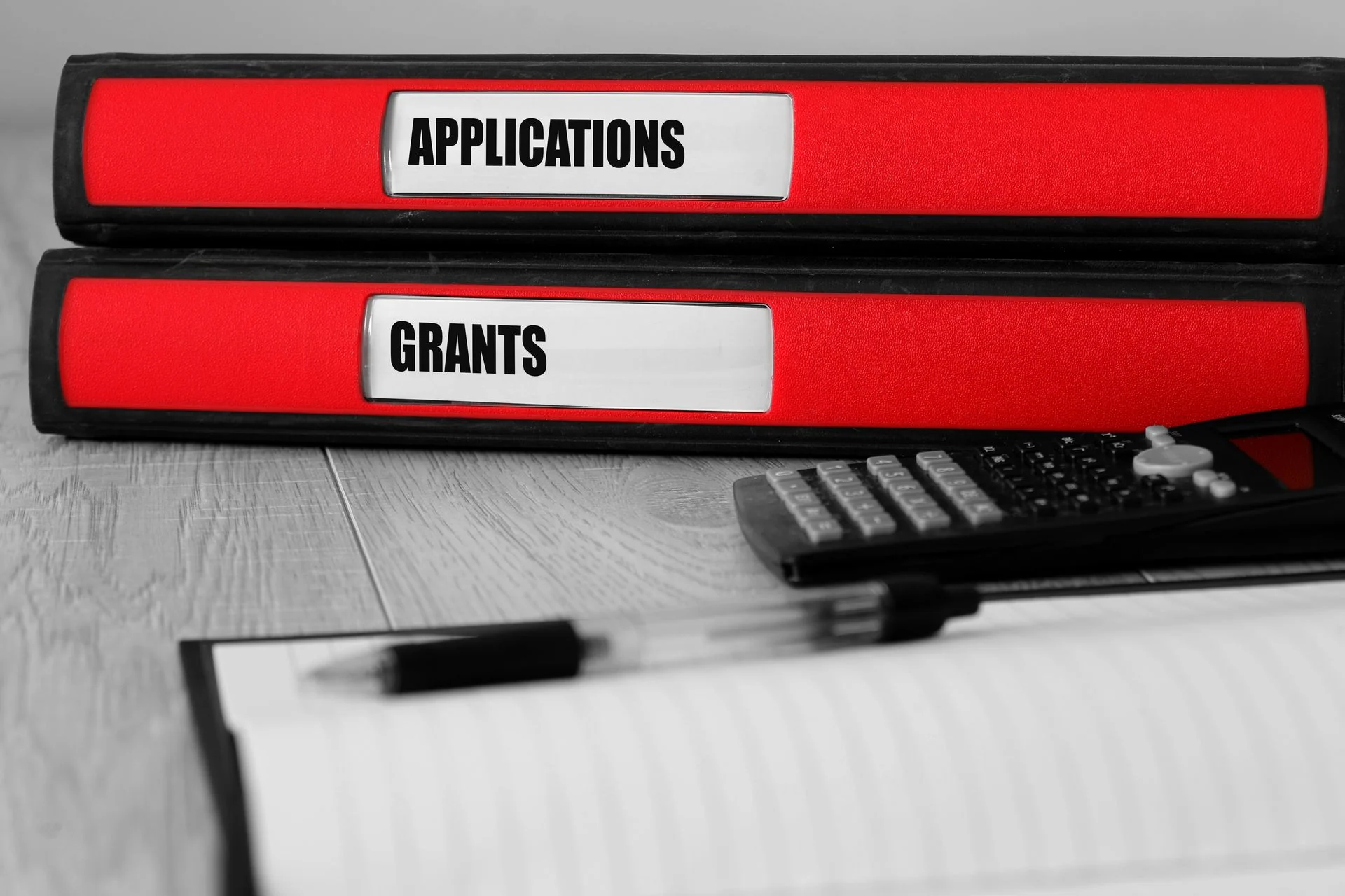 Red folders with applications and grants written on the label on a desk with selective colour